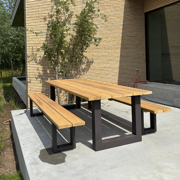 tuintafel van iroko hout met stalen U poten zwart gepoedercoat in tuin op beton ondergrond