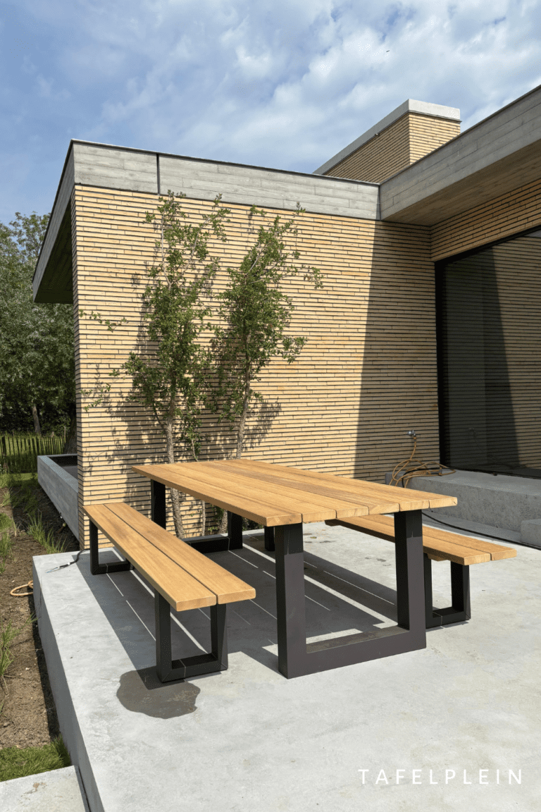 tuintafel van iroko hout met stalen U poten zwart gepoedercoat in tuin op beton ondergrond