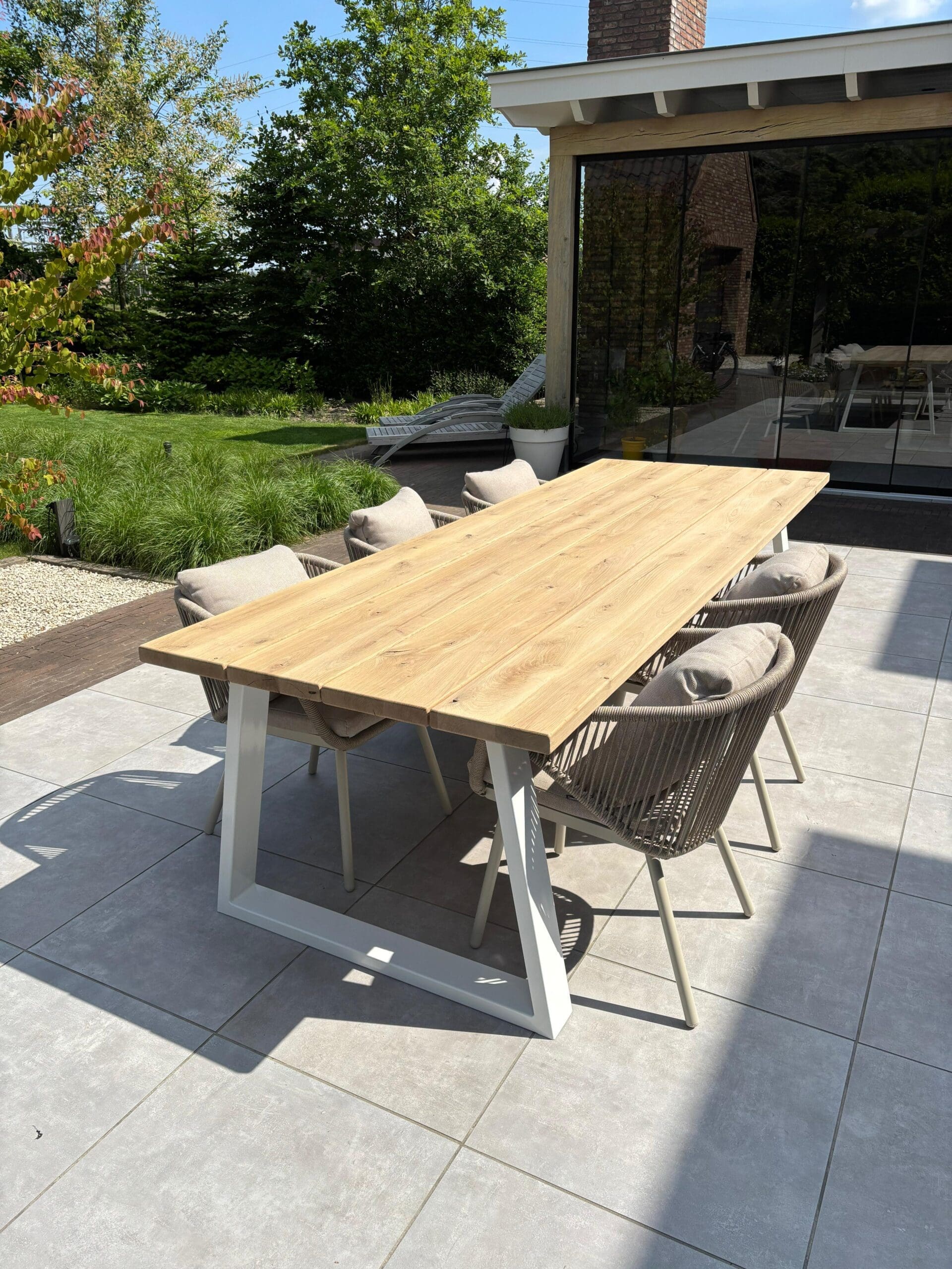 Tuintafel met stalen witte trapeze poten van eiken hout op een terras met tuinstoelen